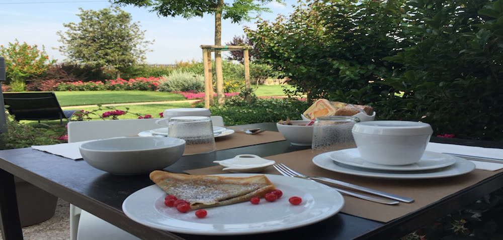 Tavolo della colazione apparecchiato in giardino con crêpe e vista sul verde