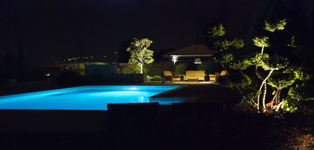Piscina illuminata di sera con gazebo e luci in giardino