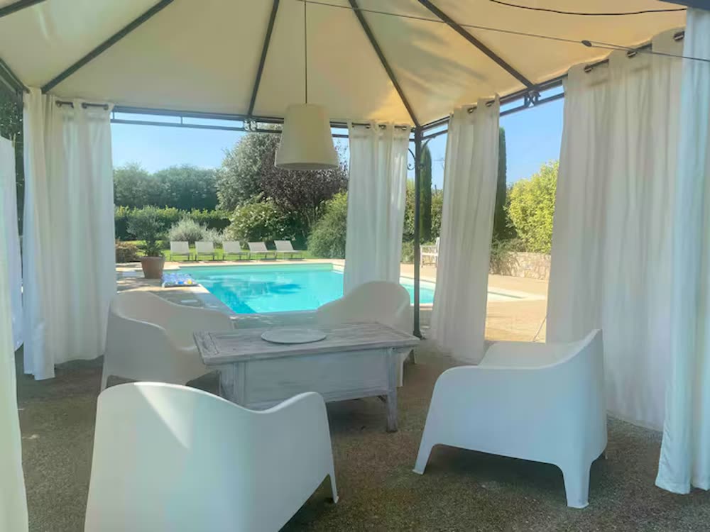 Angolo lounge coperto con tende bianche a bordo piscina